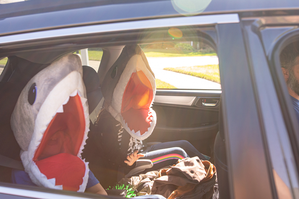 Two kids in shark costumes sitting in the backseat of a car