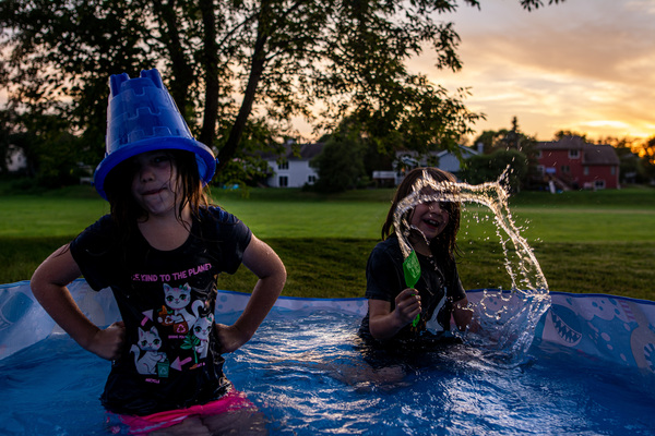 Girl with bucket on her head playing in the pool with her brother